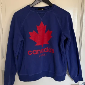Blå sweatshirt från Dsquared2 - Cool blå sweatshirt från Dsquared2 med stort rött lönnlöv och texten 'Canada's Twins' på bröstet. Tröjan har långa ärmar och rund hals. 