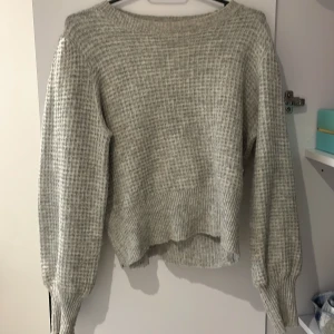 Ljusgrå stickad tröja - Mysig ljusgrå stickad tröja med ribbade muddar och avslappnad passform. Tröjan har lång ärm och är perfekt för kyligare dagar. Enkel och stilren design som passar till det mesta.