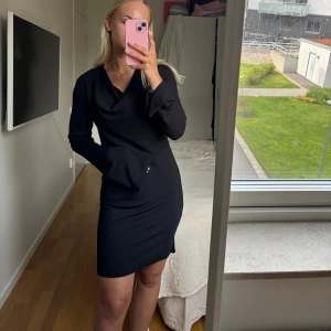 Svart långärmad klänning med v-ringning - Säljer en svart klänning med lång ärm och v-ringad hals. Klänningen har en tight passform och är i ett mjukt, stretchigt material. Perfekt för dig som gillar stilrena och enkla plagg med en elegant touch. Aldrig använd