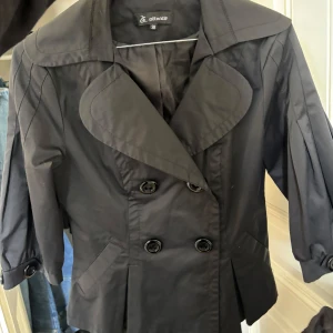 Trekvarts jacka - Snygg svart kavaj med stora slag och dubbelknäppning framtill. Jackan har trekvartsärmar med lätt puff och fickor på sidorna. Perfekt för dig som vill ha en stilren och trendig look.