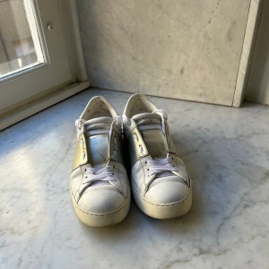 Valentino garavani - Säljer ett par vita sneakers från Valentino med ikoniska nitar runt hälen. Skorna har rund tå, platt sula och vita snören. Perfekta för dig som gillar stilrena men ändå unika detaljer.