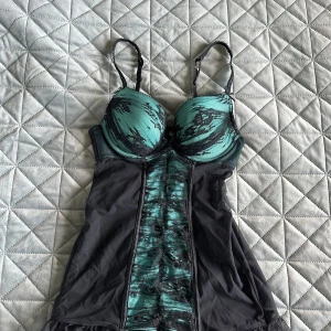 Söt korsettopp - Söt korsettopp från Ann Summers i svart och turkos. Den har justerbara axelband och strumphållare.