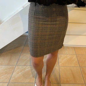 Rutig pennkjol  - Säljer en klassisk pennkjol med rutigt mönster i beige och svart. Kjolen är figurnära och har en liten slits där bak. Är i storlek 42 men passar mig i stl S/M. Har en knapp där bak och inbyggd ”satin” kjol. Går även att använda skärp till.