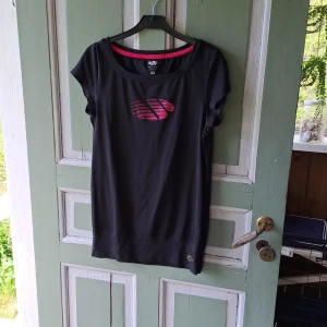 Svart sportig t-shirt från K-Swiss - Svart t-shirt från K-Swiss med rosa logga framtill. T-shirten har rund halsringning och korta ärmar. Perfekt för träning eller en sportig look. Materialet känns mjukt och lätt.