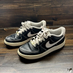 Svarta Nike sneakers med vit sula - Säljer ett par klassiska svarta Nike sneakers med vit sula och vita detaljer. Skorna har snörning och en låg profil, med vit Nike-logga på sidan och broderad text på hälen. Perfekta för en stilren vardagslook. De är limited edition.