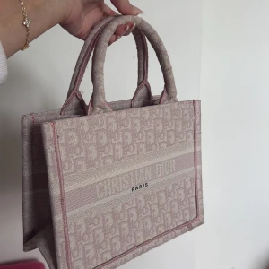 Rosa cd väska - Trendig handväska i beige och rosa med diskret mönster och texten 'PARIS' framtill. Väskan har två stadiga handtag och är tillverkad i ett tygmaterial som ger en lyxig känsla. Perfekt för att lyfta din outfit.