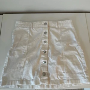 Kort jeanskjol - Säljer en superfin vit jeanskjol med knappar framtill. Den är perfekt för sommardagar och har en stilren design. Kjolen är i bra skick och passar till både vardag och fest. Ett måste i garderoben! 🌼 Skulle säga att den är lite mindre i storleken