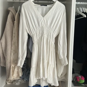 Vit långärmad klänning från Zara - Säljer en vit långärmad klänning från Zara med v-ringning och smock i midjan. Klänningen är knappast använd och det syns inte att den har användts. 
