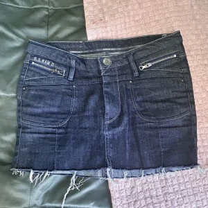Mörkblå jeanskjol från G-Star RAW - Säljer en mörkblå jeanskjol från G-Star RAW. Köpt på secondhand och använt ett par gånger men fortfarande i bra skick. Är runt 39/40 cm men är lite stretchig och passar mig som är runt 26/27 i storlek. Skriv för fler bilder och priset går att diskuteras!