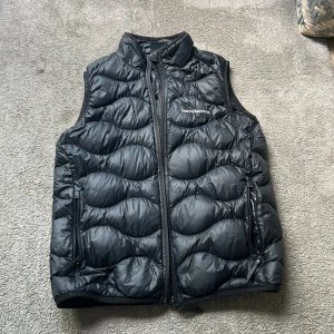 Svart dunväst från Peak Performance - Jag säljer en svart dunväst från Peak Performance, i storlek 160. Västen är använd ett fåtal gånger och har inga skador eller smuts 