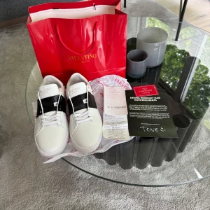 Vita sneakers från Valentino Garavani - Säljer ett par vita sneakers från Valentino Garavani med svarta detaljer och breda vita snören. Skorna har en stilren design med logotyp på plösen och en chunky sula. Perfekta för dig som gillar exklusiva och trendiga sneakers.