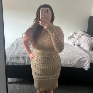 Guldig glittrig one shoulder klänning - Säljer en snygg guldig klänning med glittriga detaljer och enaxlad design. Klänningen har lång ärm på ena sidan och är figurnära med kort längd. Perfekt för dig som vill sticka ut på festen! Använd endast en gång under nyårsafton. 