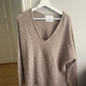 Beige stickad v-ringad tröja från Lois - Mysig beige stickad tröja från Lois med v-ringning och lång ärm. Tröjan har en avslappnad passform och är perfekt för lager-på-lager. Enkel och stilren design som passar till mycket.