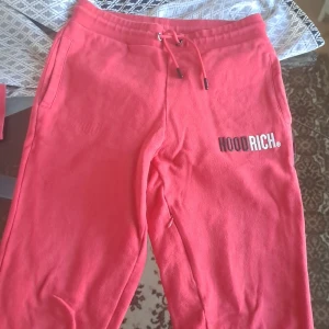 Röda mjukisbyxor från Hoodrich - Säljer ett par röda mjukisbyxor från Hoodrich med broderad logga på ena benet. Byxorna har snörning i midjan och två sidofickor. Perfekta för en avslappnad stil. Har även en liten ficka melan benet 