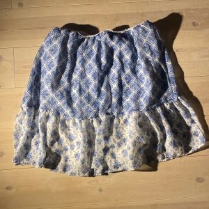 Blåvit volangkjol med mönster - Supersöt kjol i blått och vitt med två olika mönster – överdelen har ett retroinspirerat bladmönster och nederdelen är volangig med småblommigt tryck. Klänning som jag klippt av 