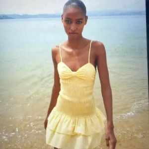 Gul Zara klänning - Supersöt trendig gul och vit rutig klänning med smala axelband, volangkjol och rosett i ryggen. Klänningen har smockad midja. Storlek xs men funkar nog för s också eftersom att den är töljlig.