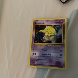 Drowzee - Drowzee är ett klassiskt Pokémon-samlarobjekt med 60 HP och två attacker: Pound och Confuse Ray. Perfekt för dig som gillar Pokémonkort och vill utöka din samling med en nostalgisk favorit.