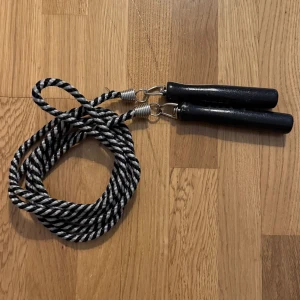 Hopprep med svarta handtag, 230 cm - Ett klassiskt hopprep med svartvita rep och svarta handtag. Perfekt för dig som vill träna kondition, koordination och smidighet på ett roligt sätt. Passar både nybörjare och erfarna. Ta med till gymmet, skolgården eller träna hemma! Repets längd 230 cm (exkl. handtag).