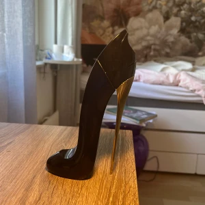 Good Girl parfymflaska i form av högklackad sko - Säljer en elegant parfymflaska från Carolina Herrera, formad som en svart högklackad sko med gulddetaljer på klacken. Flaskan har en glansig finish och är riktigt snygg som inredningsdetalj på sminkbordet. Den är dock helt tom 