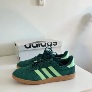 Adidas Breaknet Sleek Skor Grön - Säljer ett par Adidas Breaknet Sleek sneakers i mörkgrön mocka med ljusgröna klassiska ränder. Skorna har snörning och Cloudfoam Plus-innersula. De är helt nya med inga utseendedefekter, då jag köpte en för stor storlek. Stilrena och snygga skor som passar till sommarens outfits!💚🌟