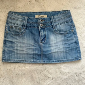 Blå jeanskjol från Monday - Säljer en klassisk blå vintage jeanskjol från Monday med fem fickor och bälteshällor. Kjolen har en kort passform och stängs med knapp och dragkedja framtill.