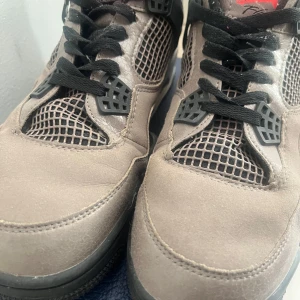 Nike Air Jordans i grå mocka med svarta detaljer - Säljer ett par Nike Air Jordans i grå mocka med svarta detaljer och röd insida. Skorna har svarta snören, meshpaneler och den klassiska Jumpman-loggan på hälen och plösen. Perfekta för dig som gillar streetwear och sneakers med attityd.