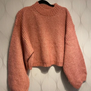 Rosa stickad croppad tröja från Gina Tricot - Superfin rosa stickad tröja från Gina Tricot i croppad modell. Tröjan har breda ärmar, ribbad struktur och hög halsringning. Perfekt för lager på lager och ger en mysig vibe till din outfit.