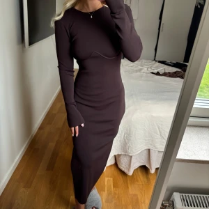 Mörkbrun långklänning med öppen rygg - Säljer en mörkbrun långklänning med lång ärm och öppen rygg. Klänningen har en tight passform och är tillverkad i ett ribbat material som sitter snyggt på kroppen. Perfekt för dig som gillar stilrena och trendiga plagg.