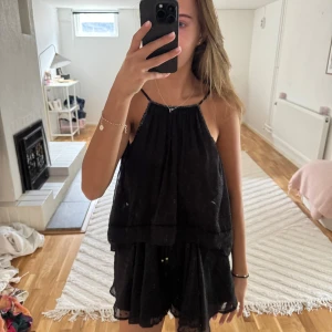 Svart kortklänning med tunna axelband - Säljer en svart kortklänning med tunna axelband och lös passform. Klänningen har dubbla lager tyg och en luftig känsla, perfekt för varma dagar. Enkel och stilren design som passar till många tillfällen. Finns shorts i klänningen 