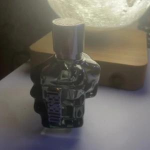 Diesel Only The Brave Eau de Toilette - Parfymflaska formad som en knytnäve i genomskinligt glas med silvrig metallkork. Märket Diesel syns tydligt på flaskan. Doften är känd för sina fräscha och maskulina toner.