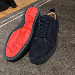 Mörk blå Christian Louboutin - Säljer ett par mörkblå sneakers i mocka från Christian Louboutin med ikonisk röd sula och broderad logga på hälen. Skorna har rund tå, platt sula och snörning. Perfekta för dig som vill sticka ut med stilrena detaljer.