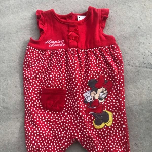 Röd prickig jumpsuit med Minnie Mouse - Supersöt röd jumpsuit med vita prickar och broderad Minnie Mouse framtill. Junpsuiten har ärmlös design, liten ficka och fina rosettdetaljer vid halsen. Perfekt för dig som älskar Disney och vill sticka ut med en färgglad look.