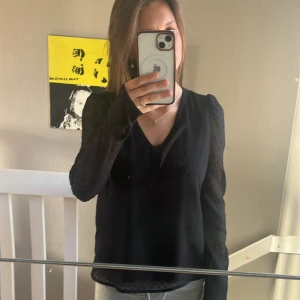 Svart blus med diskreta prickar - Säljer en svart blus med v-ringning och långa ärmar. Blusen har ett diskret prickigt mönster i tyget och är lätt transparent på ärmarna. Perfekt för dig som vill ha en stilren men ändå unik topp.