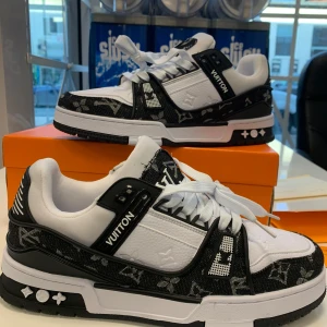 Louis Vuitton trainers  - Säljer ett par Louis Vuitton sneakers i svart och vitt med klassiskt monogrammönster. Skorna har snörning, rund tå och platt sula. Märkeslogga syns tydligt på sidan, sulan och plösen. Perfekta för dig som vill sticka ut med lyxiga detaljer.