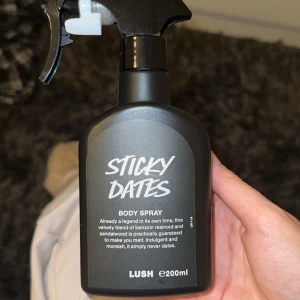 Sticky Dates Body Spray från Lush - Säljer en Sticky Dates Body Spray från Lush i svart plastflaska med spraymunstycke. Doften har inslag av benzoin och sandelträ, vilket ger en söt och varm känsla. Flaskan rymmer 200 ml och har en modern, stilren design. Använd 3 gånger ungefär