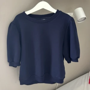 Mörkblå tröja med puffärmar från Gina Tricot - Säljer en mörkblå tröja från Gina Tricot med puffiga korta ärmar och ribbade muddar vid hals, ärmslut och nederkant. Enkel och stilren modell som passar till mycket. Perfekt för dig som gillar en klassisk look med en twist.