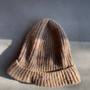 Brun ribbad mössa från CW by Carin Wester - Mysig brun ribbstickad mössa från CW by Carin Wester. Klassisk modell med uppvikt kant och diskret logga framtill. Perfekt för kyliga dagar och enkel att matcha med olika outfits.