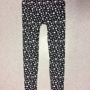 Super Stretch leggings med vita stjärnor - Säljer ett par svarta leggings med vita stjärnor över hela byxan. De är tighta och har en elastisk midja som gör dem bekväma att bära. Perfekta för dig som gillar mönstrade plagg och vill sticka ut lite extra. Stlk S-L 