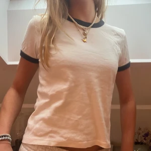 Vit t-shirt med blå detaljer  - Säljer en vit t-shirt med blå kanter vid ärmslut och halsringning. T-shirten har en klassisk passform och är kortärmad, perfekt till jeans eller shorts. Enkel och stilren design som passar till många tillfällen. 