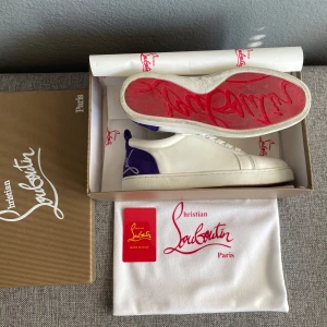 Louboutin Vit/lila - Säljer ett par exklusiva vita sneakers. Nästan sprillans nya, skick 9,5/10, sitter extremt bra och passar till många outfits, storlek 39 men passar även 40 bra, skriv vid intresse av köp!😃