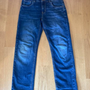 Blå jeansbyxor från LAB Industries - Säljer ett par klassiska blå jeansbyxor från LAB Industries med regular fit och retrostil. Byxorna har fem fickor, knapp och dragkedja framtill samt snygga slitningar för en vintage look.