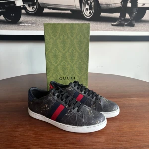 Gucci sneakers - Säljer ett par Gucci sneakers i mörkgrått med klassiskt GG-mönster, röda och blå ränder på sidorna samt olika färg på hälen – en röd och en blå. Skorna har vit platt sula och svarta skosnören. Perfekt för dig som vill sticka ut med lyxig stil. Inga defekter och nypris ligger på 9000!