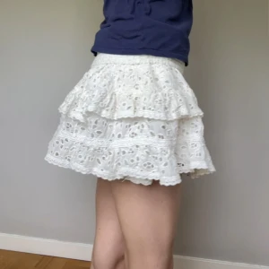 Vit volangkjol med broderade detaljer från odd molly - Supersöt vit kjol med flera lager volanger och broderat mönster. Kjolen har resår i midjan och knytband framtill. Brukar vika ner den högst upp!! Den är från odd molly och passar storlek S/M, och 100% cotton