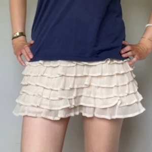 Beige volangkjol med resårmidja - Supersöt beige minikjol med flera lager volanger och resår i midjan. Kjolen har en luftig och lätt känsla, perfekt för sommaren! Den är från märket madonna och är cirka storlek XS/S