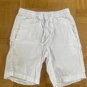 Vita linneshorts från Skagen - Säljer ett par fräscha vita shorts från Skagen i 100% linne. De har elastisk midja med snörning, två sidofickor och en bakficka. Perfekta för varma dagar och har en avslappnad passform. Går att diskutera priset