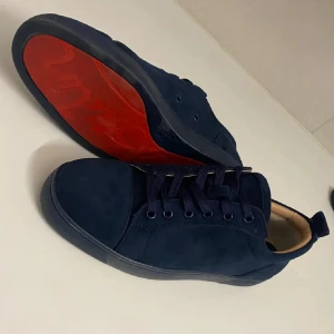Christian Louboutin  - Snygga mörkblå sneakers från Christian Louboutin med ovandel i mocka och klassisk röd sula. Skorna har rund tå, platt sula och snörning framtill. Perfekta för dig som vill sticka ut med en exklusiv touch. Inge box tyvärr där av priset 
