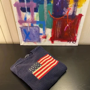 Mörkblå stickad tröja med amerikansk flagga - Mörkblå stickad tröja med en stor amerikansk flagga framtill. Tröjan har rund halsringning och långa ärmar. Perfekt för dig som gillar klassisk och preppy stil.