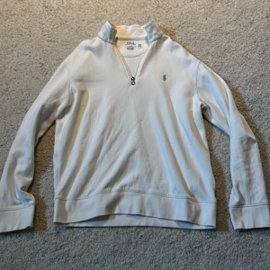 Vit halvzip tröja från Polo Ralph Lauren - Säljer en vit långärmad tröja från Polo Ralph Lauren med halv dragkedja och den klassiska broderade loggan på bröstet. Tröjan har en klassisk passform och är tillverkad i mjuk bomull. Perfekt för en stilren och avslappnad look. Skick 8/10