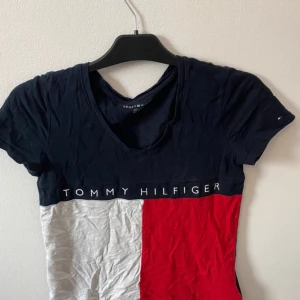 Flerfärgad t-shirt från Tommy Hilfiger - Säljer en snygg t-shirt från Tommy Hilfiger i färgerna marinblå, vit och röd. T-shirten har korta ärmar, v-ringning och klassisk logga framtill. Perfekt för en stilren och sportig look.Frakt tillkommer