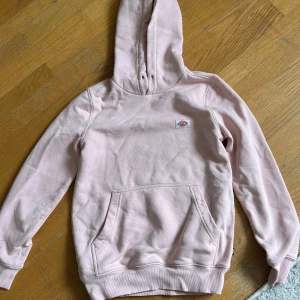 Ljusrosa hoodie från Dickies - Säljer en ljusrosa hoodie från Dickies med klassisk känguruficka och liten logga på bröstet. Tröjan har huva och långa ärmar, perfekt för en avslappnad stil. Mjuk och skön att ha på sig.